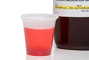 Liquid medication in a cup sits next to a bottle.