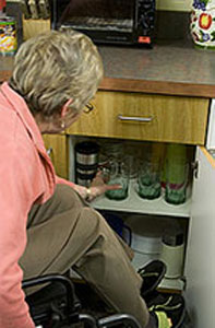 a woman in a wheelchair reaches for a glass in a lower cabinet