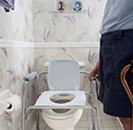 a man with a cane approaches a toilet with grab bars